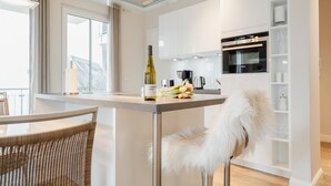 A modern kitchen with white cabinets, a built-in oven, and a glass-top dining table.