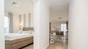 A modern hotel room with a bed, a desk, and a kitchenette.