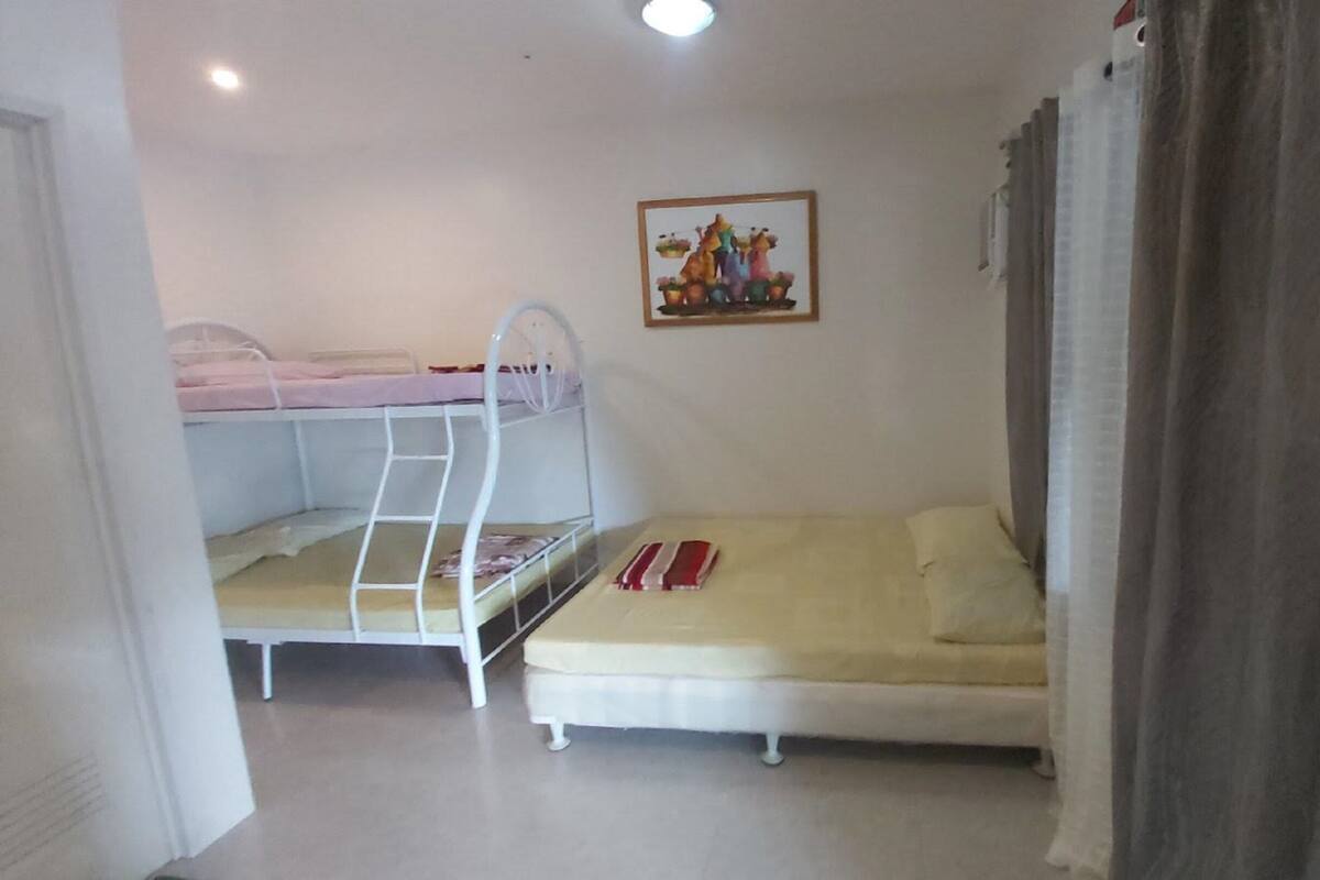 Une chambre avec des lits superposés et un lit simple, un tableau au mur et un rideau à la fenêtre.