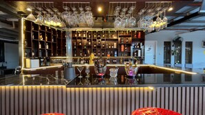 Un espace bar doté d’un comptoir noir poli, d’étagères remplies de bouteilles et de verres suspendus.