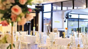 Une salle de banquet avec des chaises et des tables blanches, de grandes fenêtres et un système de sonorisation.