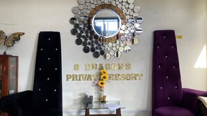 Une pièce avec un grand miroir mural, entouré de petits miroirs ronds, deux fauteuils rembourrés, une petite table avec un vase et une pancarte indiquant : « 8 Dragons, complexe privé ».