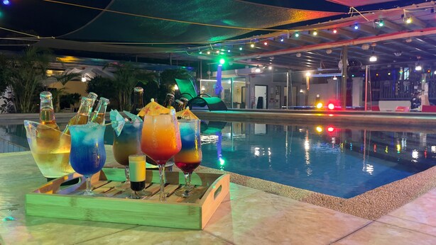 Un espace aménagé au bord de la piscine, avec un bar en bois où sont servis différents cocktails colorés.