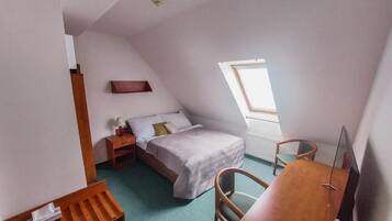 A small, well-lit room with a bed, a desk, and a window.