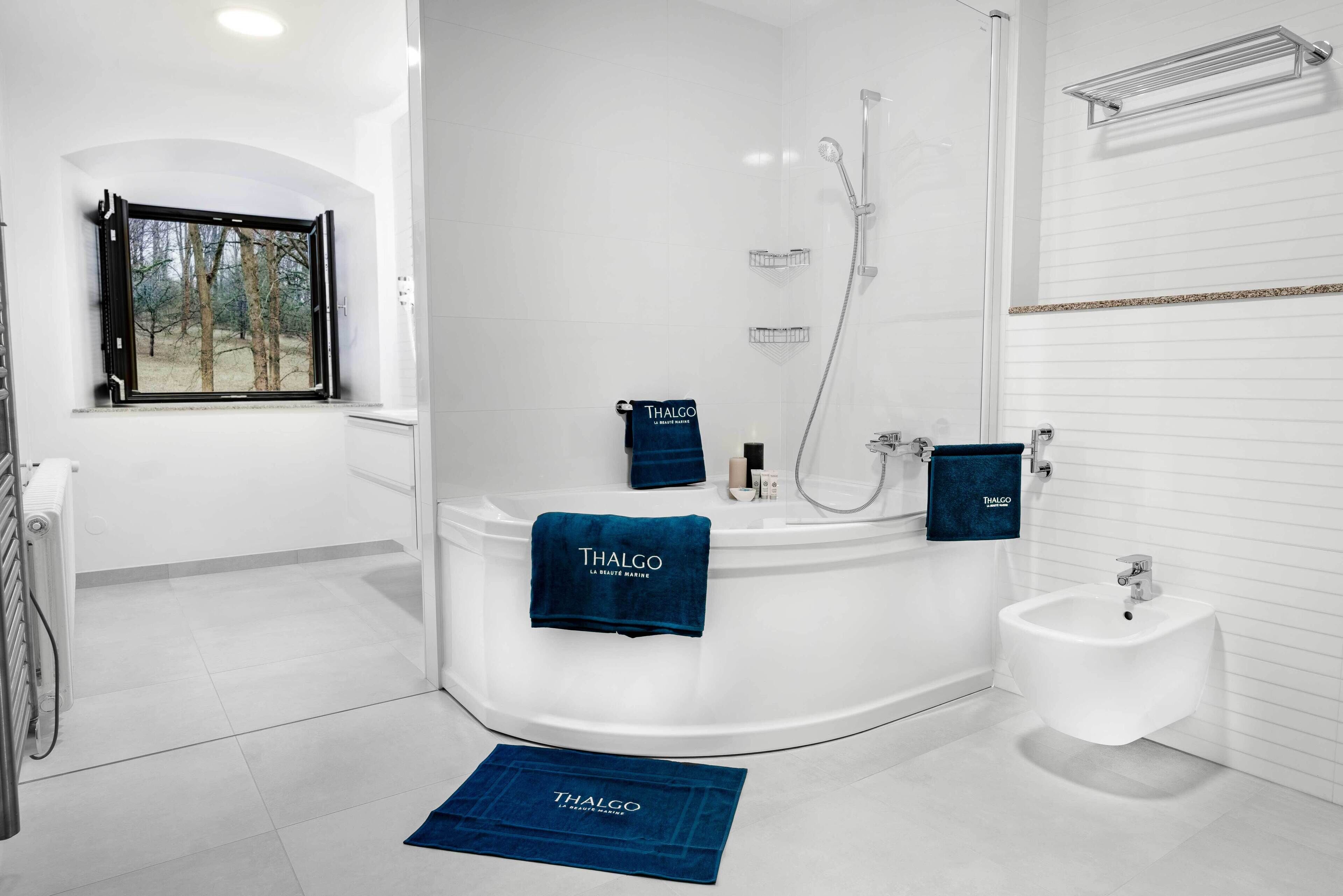Un baño moderno con bañera, bidé y ventana con vista a árboles.