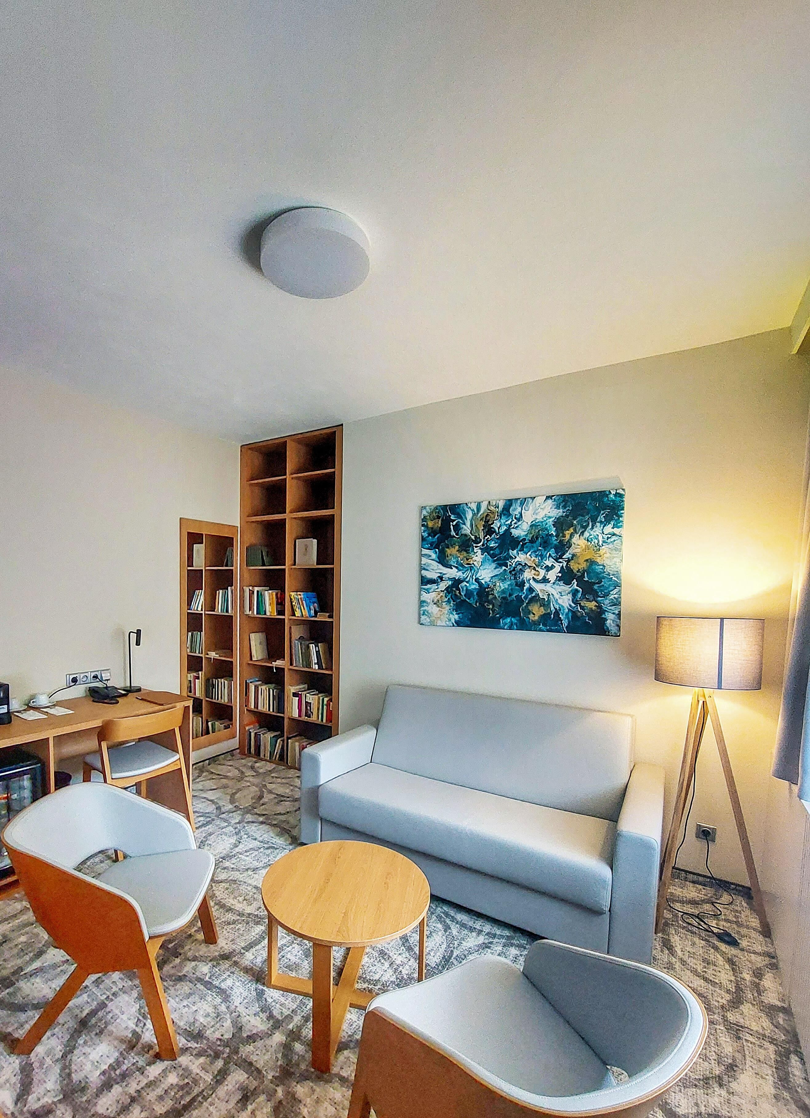 Un salon comprenant un canapé, deux fauteuils, une table basse, une bibliothèque, un tableau et une lampe.