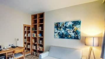 Un salon comprenant un canapé, deux fauteuils, une table basse, une bibliothèque, un tableau et une lampe.