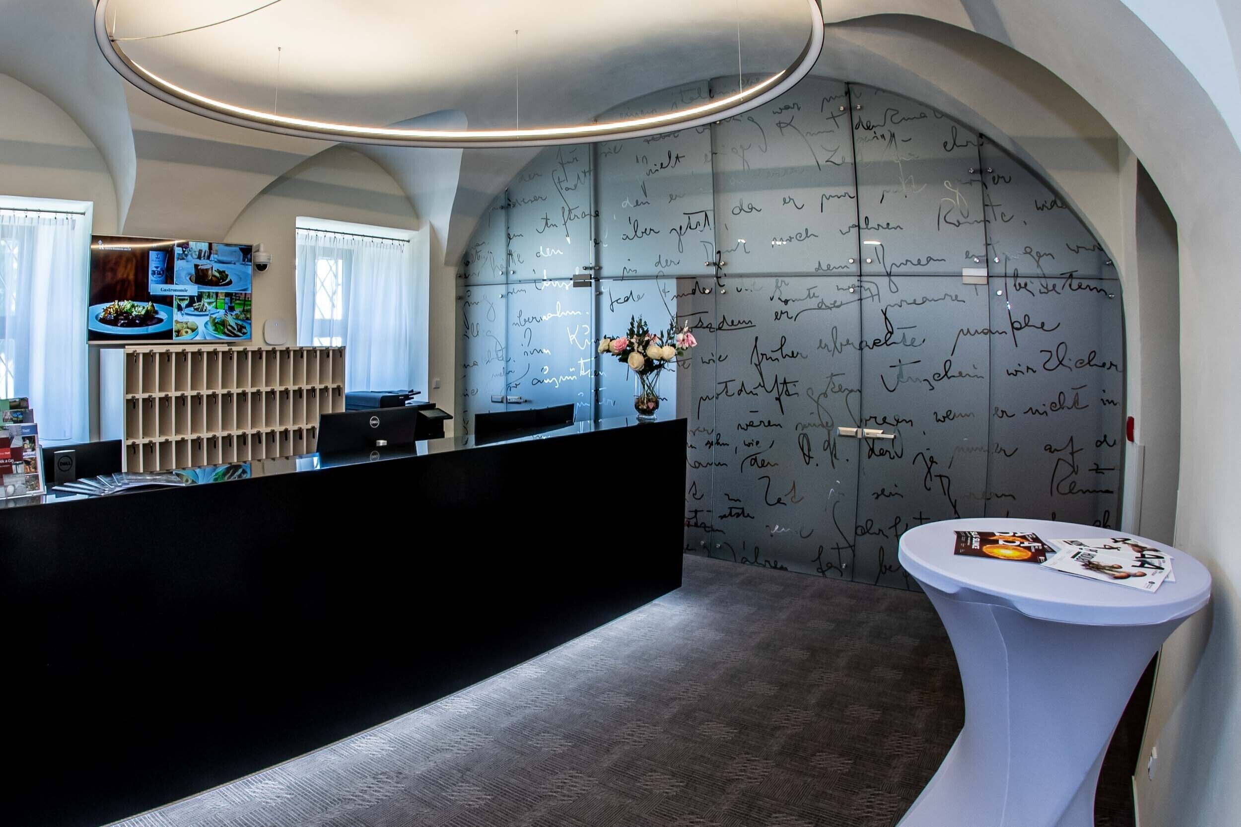 A reception area with a black reception desk, a white side table, and a wall with handwritten notes.