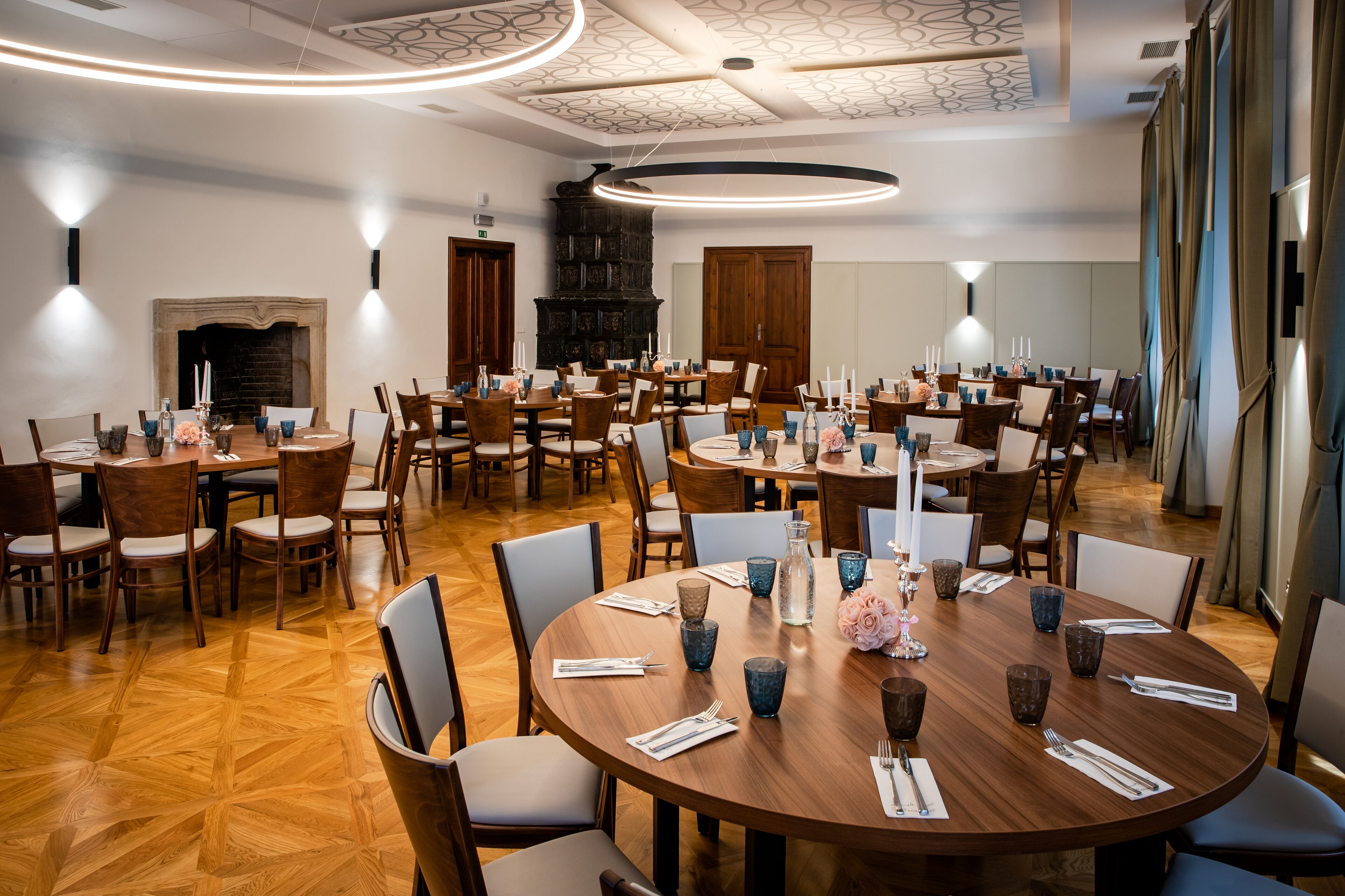 A spacious dining area with multiple round tables, each set with chairs, candles, and blue glassware.