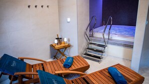 A spa room with wooden loungers, a small table with a towel, and a view of a hot tub. - Chateau Třešť (Trest)