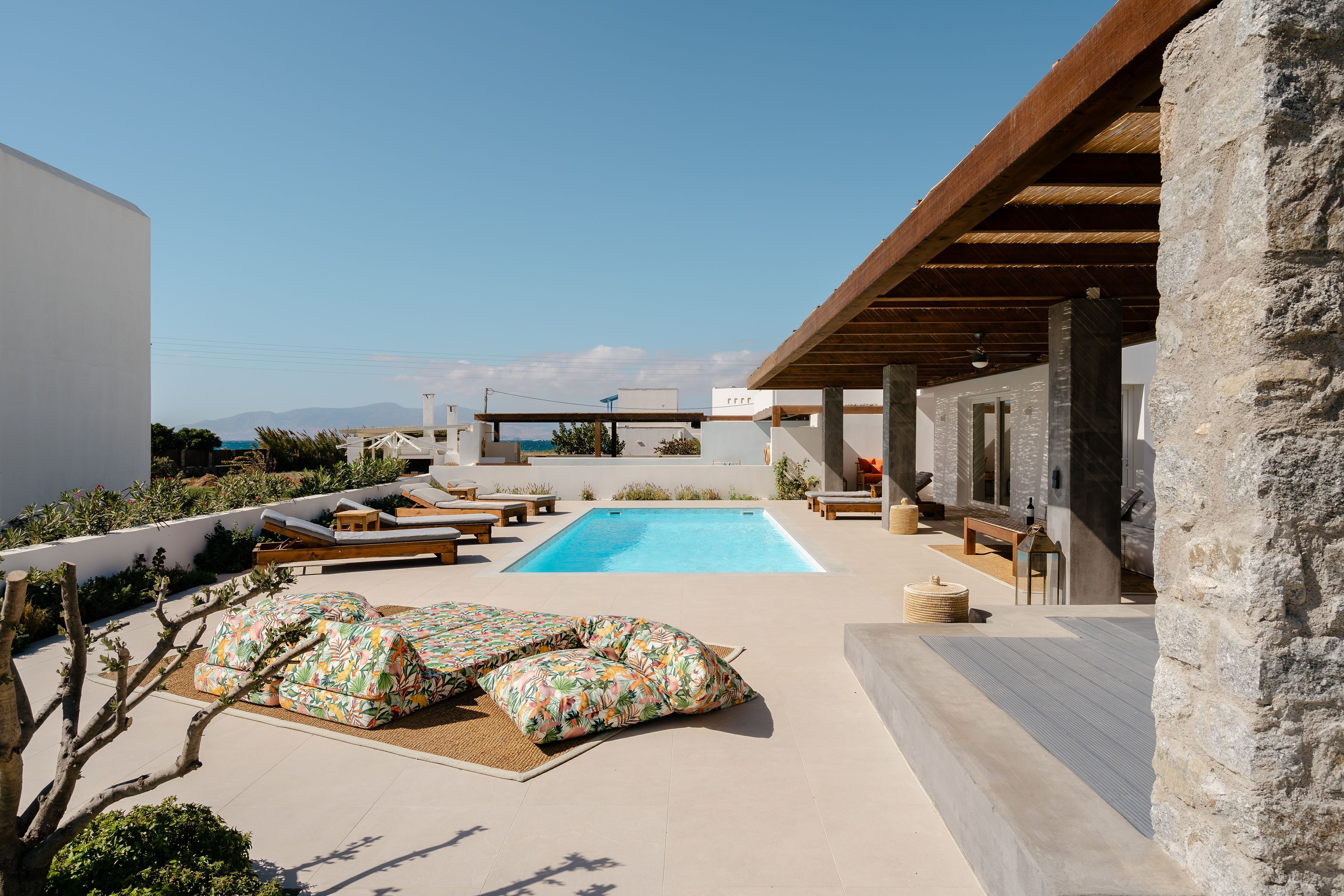 A rooftop pool area with a clear view of the sea, lounge chairs, and a stone pillar.