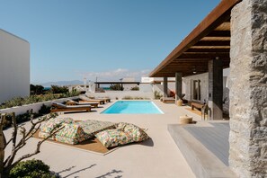 A rooftop pool area with a clear view of the sea, lounge chairs, and a stone pillar. - Citrus Seaside Houses (Naxos)