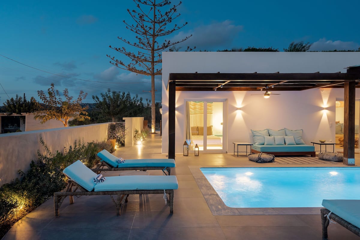 A modern outdoor pool area with lounge chairs and a sofa, surrounded by a low wall and vegetation.