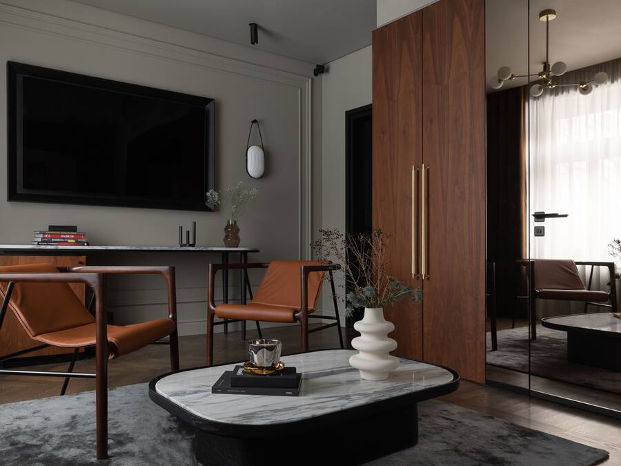 A modern living room with a large flat-screen TV, two leather chairs, a marble coffee table, and a wooden cabinet.