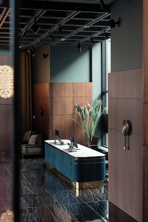 A modern reception area with a marble floor, a reception desk, a potted plant, and a large window. - A22 Hotel (Riga)