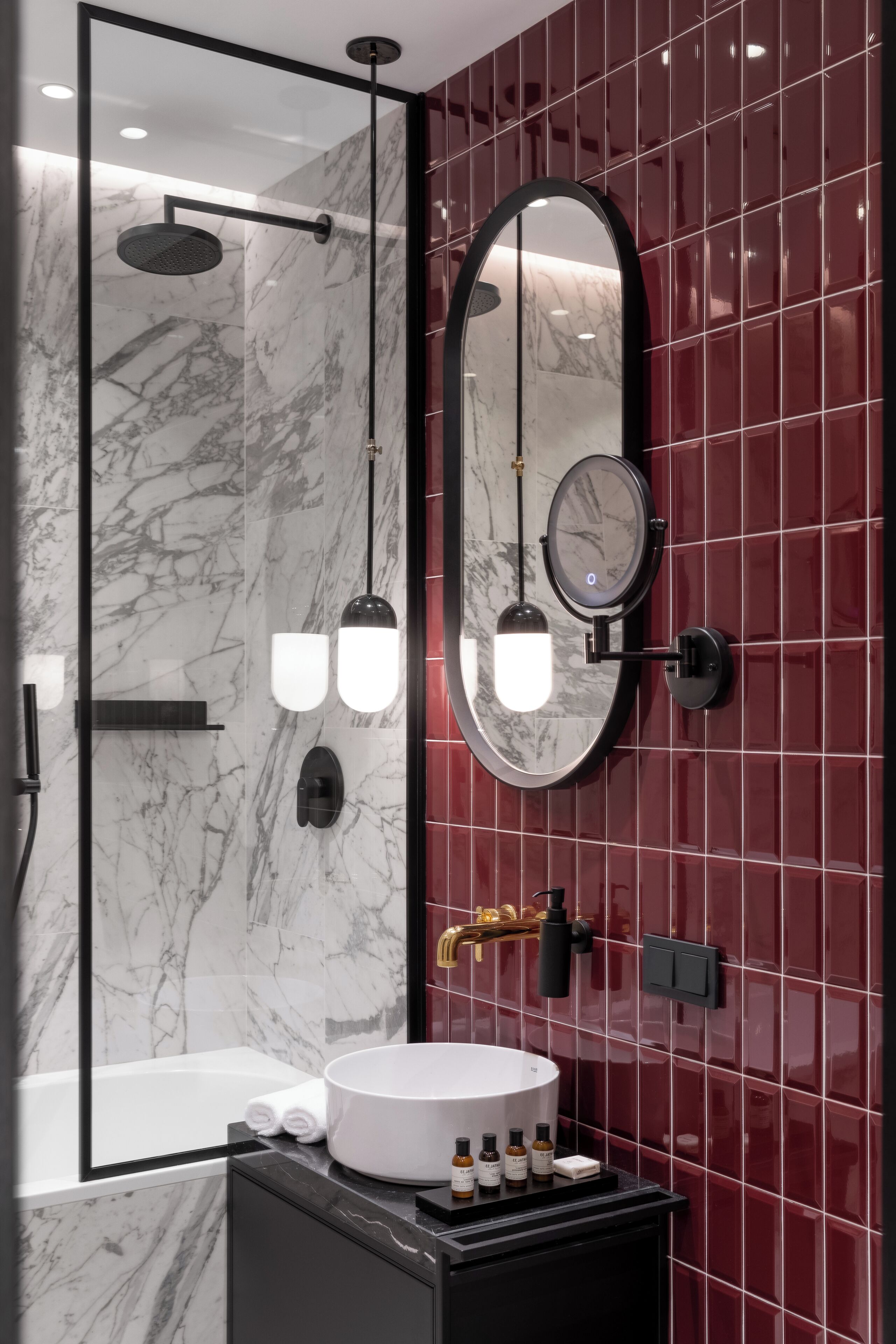 A modern bathroom with a marble wall, a round mirror, a white sink, and a handheld showerhead.