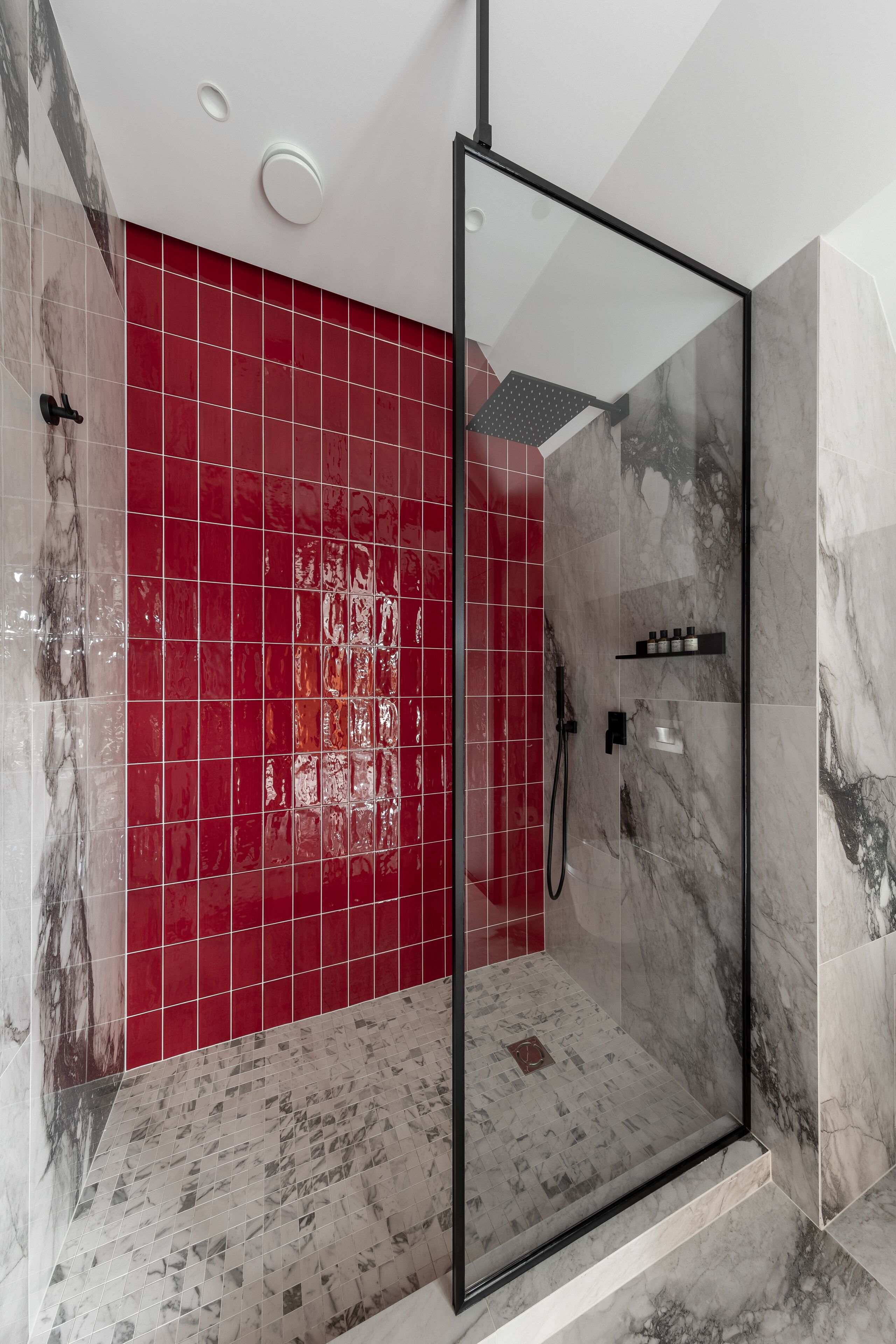 Una ducha moderna con puerta de vidrio, azulejos rojos y suelo de mármol.
