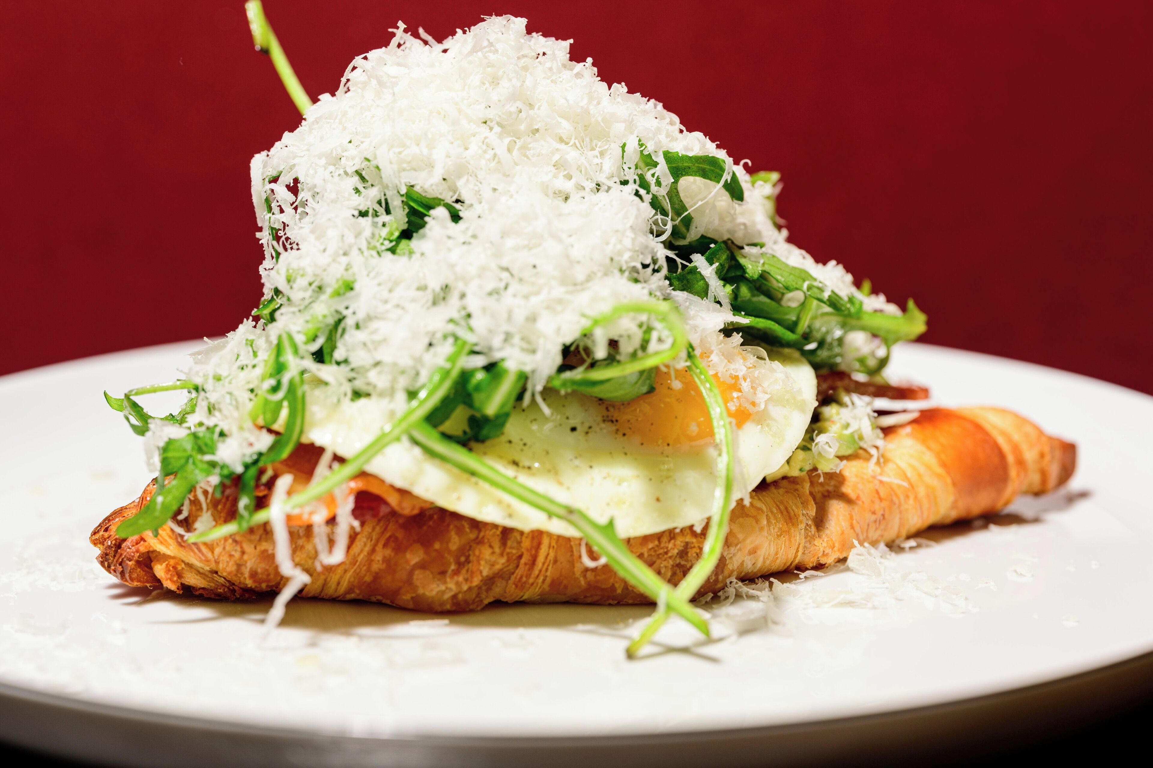 A plate with a croissant, egg, greens, and cheese.