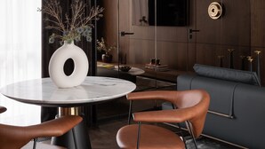 Een moderne woonkamer met een ronde tafel, twee bruine leren fauteuils, een donkere bank en een grote flatscreen-televisie aan de muur.