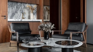 En moderne stue med to læderstole, et marmorbord, en vase med tørrede blomster og et træskab med marmorbeklædt bagside.