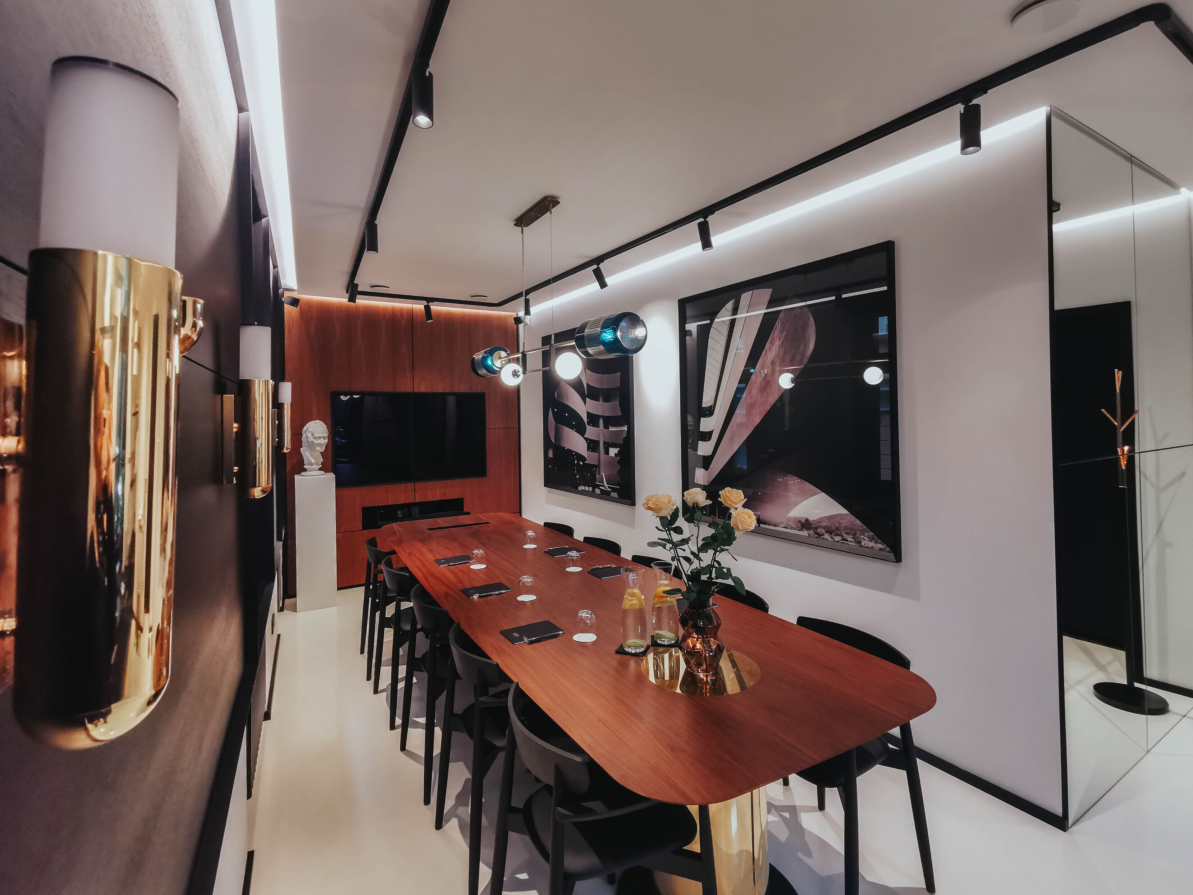 A modern dining area with a long wooden table, black chairs, and a large flat-screen TV on the wall.