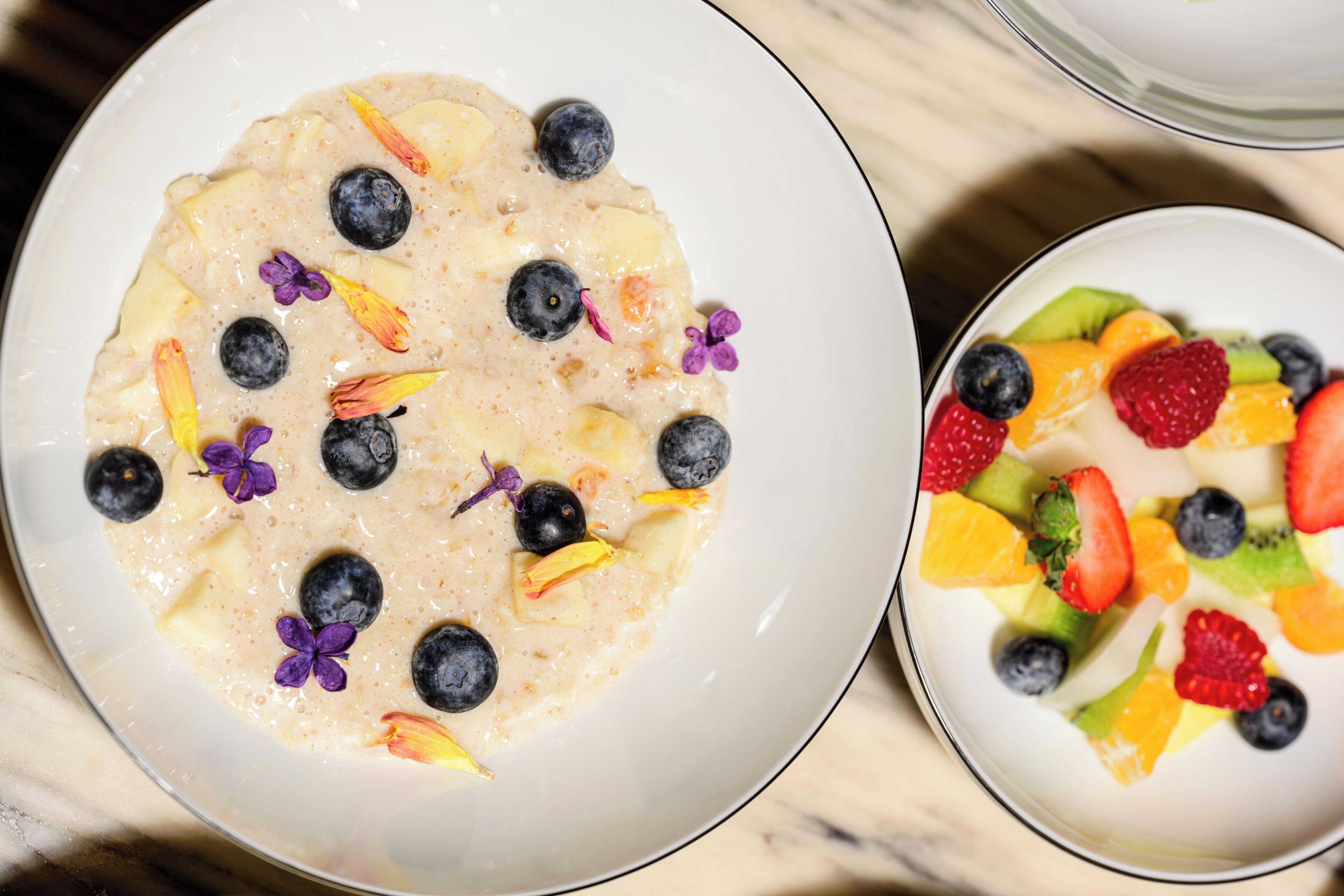 Two bowls of food, one with oatmeal and fruit, and the other with a variety of fresh fruits.