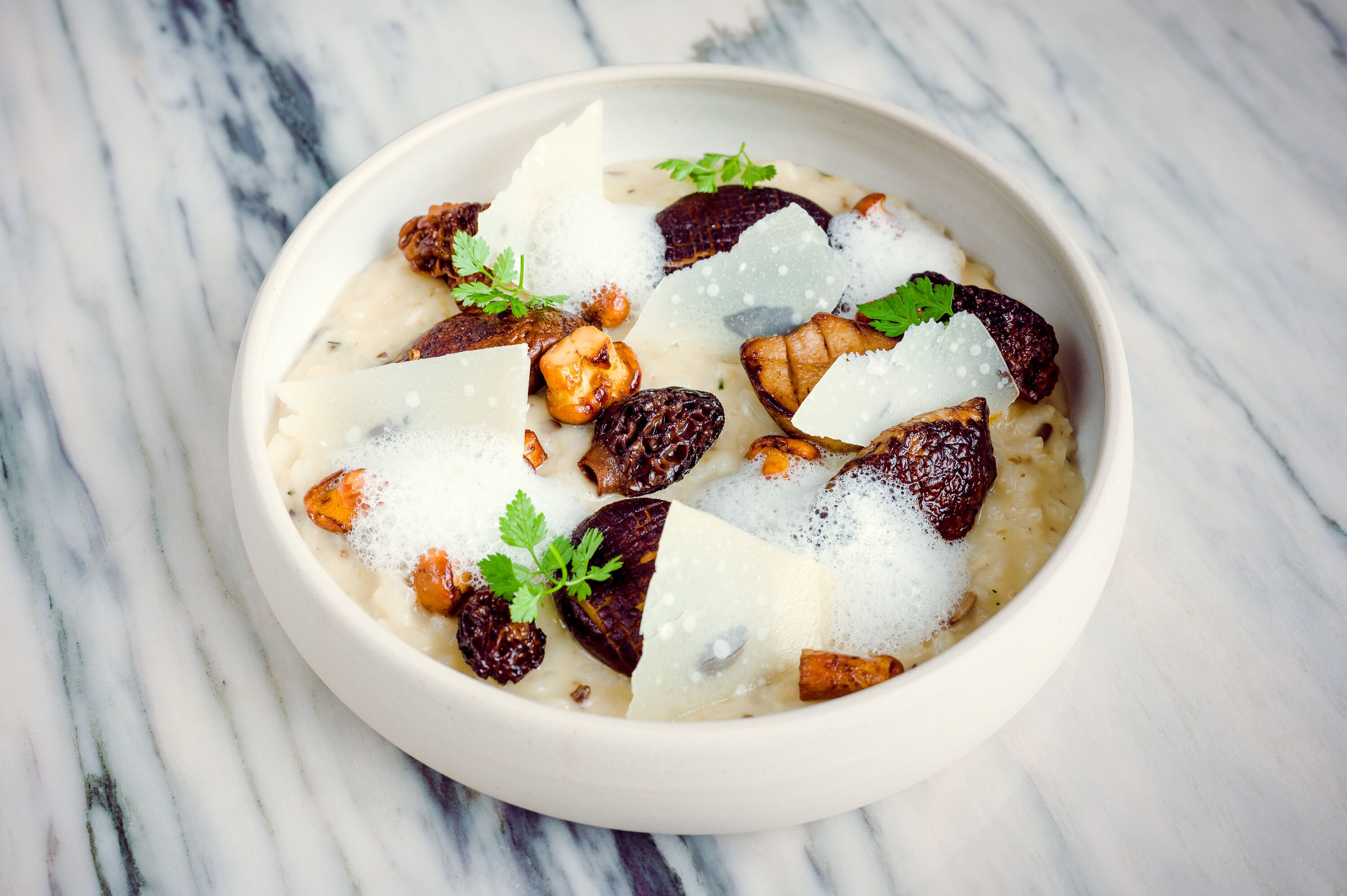 A bowl of food with figs, nuts, and cheese on a marble surface.
