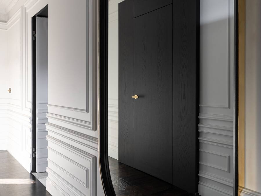 A hallway with a dark wooden door and a large mirror reflecting the door.