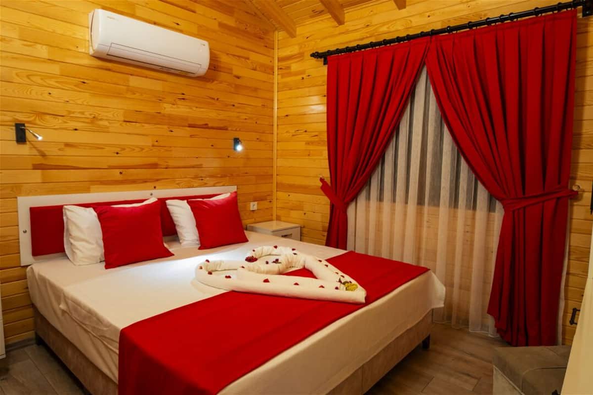 Quarto com painéis de madeira, uma cama, cortinas vermelhas e um ar condicionado branco.