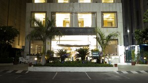 A modern hotel with a prominent neon sign, multiple illuminated windows, and a well-lit entrance area with outdoor seating and plants. - Alivaa Hotel, Millennium City Center, Sector 29, Gurugram (Gurugram)