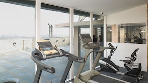 A gym with treadmills and exercise bikes, large windows, and a view of the city. - Alivaa Hotel, Millennium City Center, Sector 29, Gurugram (Gurugram)
