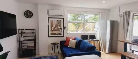 A modern living room with a sofa, a coffee table, a TV, a clock, and a window with a view of the outdoors.