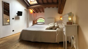 Une chambre avec un grand lit, une lucarne, une table de chevet avec une lampe et une vue sur la verdure à l’extérieur.