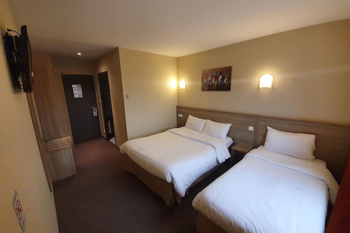 A hotel room with two single beds, a wooden headboard, a wall-mounted TV, and a painting above the bed.