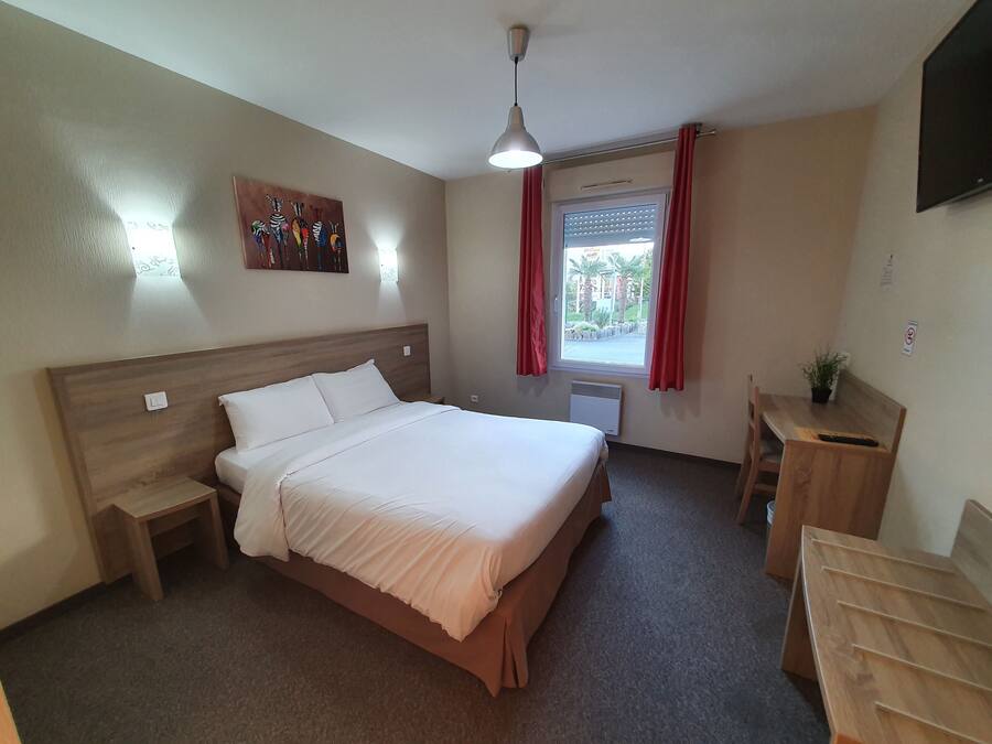 A bedroom with a bed, bedside tables, a desk, a chair, a window with curtains, a ceiling light, and a wall-mounted TV.
