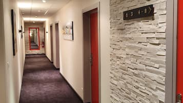 En hotellkorridor med en vägg som har ett mönster, röda dörrar och en skylt som visar vägen.