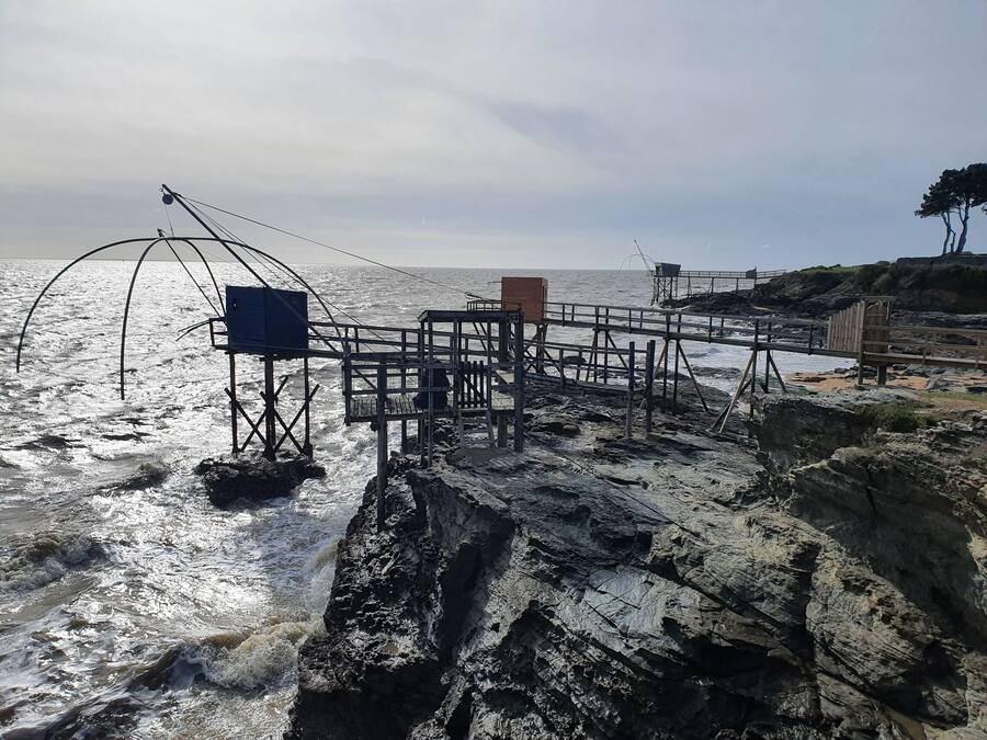 A pier extending into the sea with a metal structure and a blue sign.