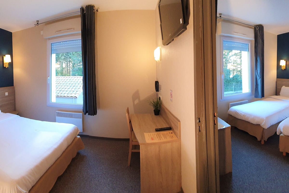 A hotel room with two single beds, a desk, a chair, a TV, and artwork on the walls.