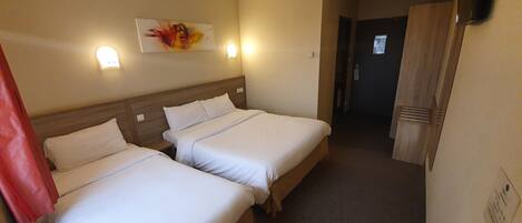 A hotel room with two beds, a wooden headboard, a painting on the wall, a TV mounted on the wall, and a wooden table with a remote control on it.