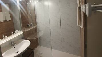 A modern bathroom with a large mirror, two sinks, a shower, and a towel rack.