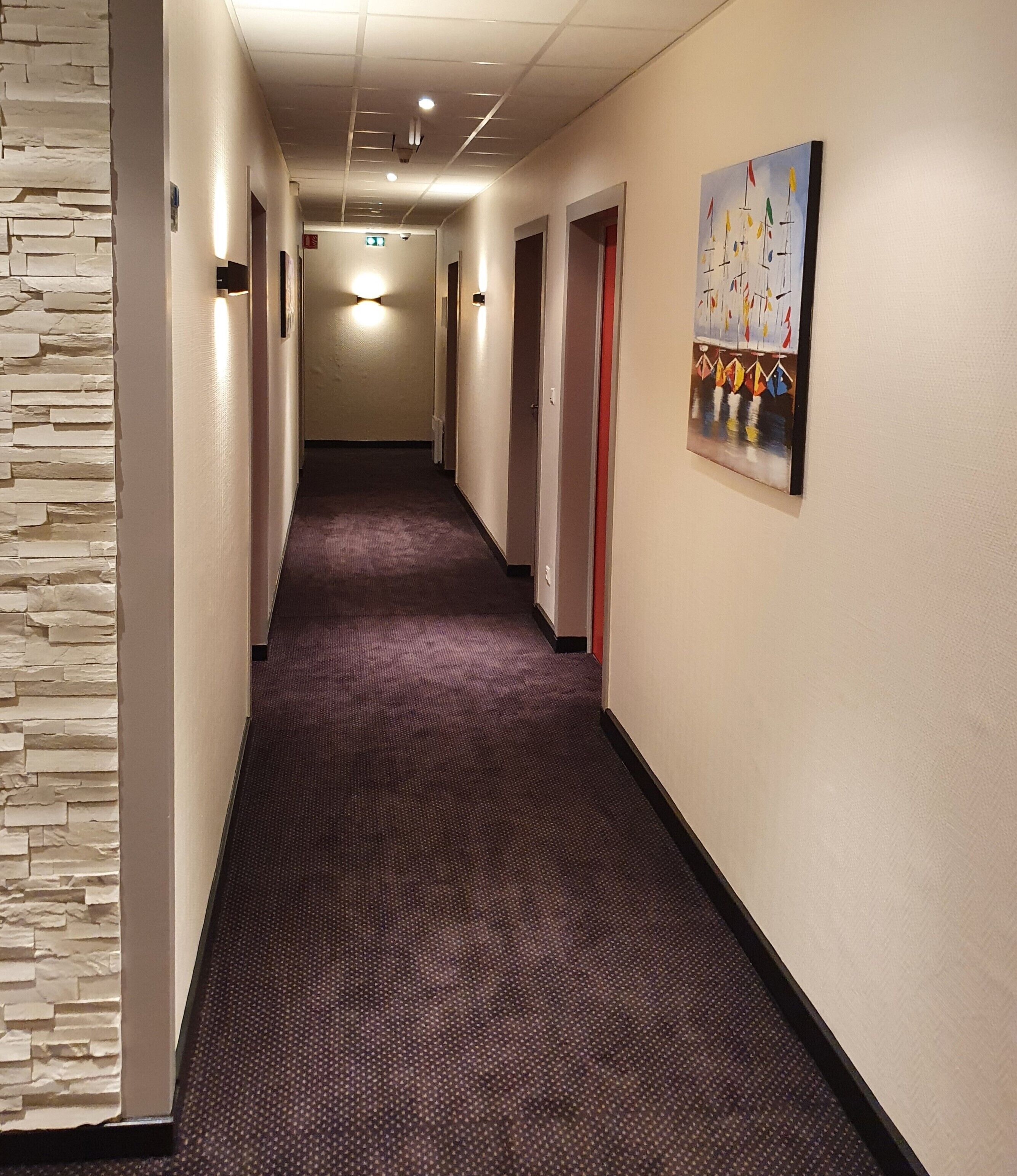 A hotel hallway with a stone accent wall, a patterned carpet, and a painting on the wall.