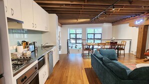 A modern kitchen with white cabinets, a gas stove, and a dishwasher. There is a dining area with a wooden table and chairs, and a sofa in the living room. - Central New York-Style Loft with parking - Inner City Apartment - Chippendale (Chippendale)