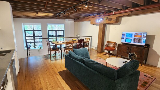 A modern kitchen with a stainless steel stove, a dining area with a wooden table and chairs, a blue sofa, and a television on a wooden cabinet. - Central New York-Style Loft with parking - Inner City Apartment - Chippendale (Chippendale)