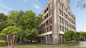 A multi-story building with a prominent corner entrance, large windows, and a brick facade. - Central New York-Style Loft with parking - Inner City Apartment - Chippendale (Chippendale)