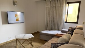 Una sala de estar moderna con un sofá, un reposapiés y un televisor montado en la pared.