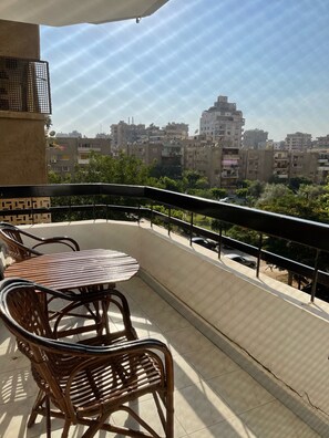 Un balcon avec une table et des chaises, donnant sur un paysage urbain composé de nombreux immeubles.