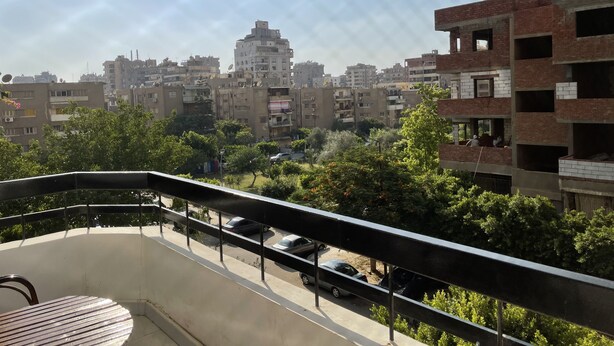 Un balcón con vistas a un paisaje urbano, incluyendo edificios de varios pisos y coches aparcados.