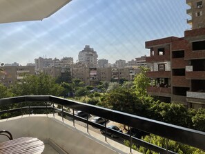 Un balcón con vistas a un paisaje urbano, incluyendo edificios de varios pisos y coches aparcados.