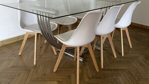 Un comedor moderno con una mesa de vidrio rodeada de sillas blancas con patas de madera.