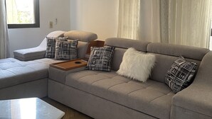 Una sala de estar moderna con un sofá modular gris, piso de madera en patrón de espiga, una mesa de centro de vidrio y una araña.